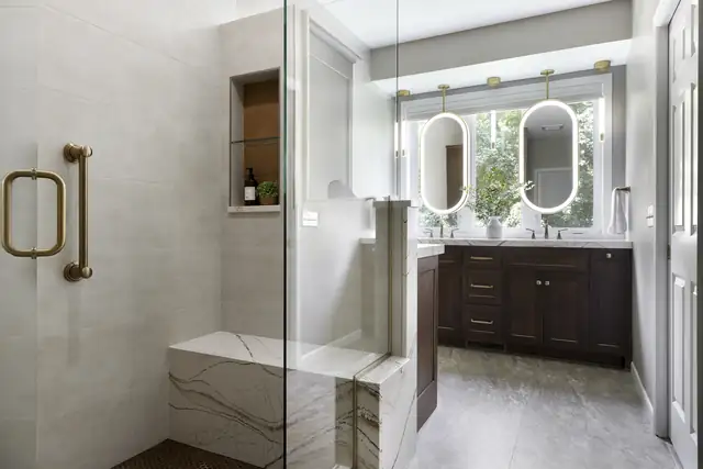 Lakeville primary bath remodel with walk-in shower, quartz bench, brass handle and dark cherry vanity with illuminated mirrors